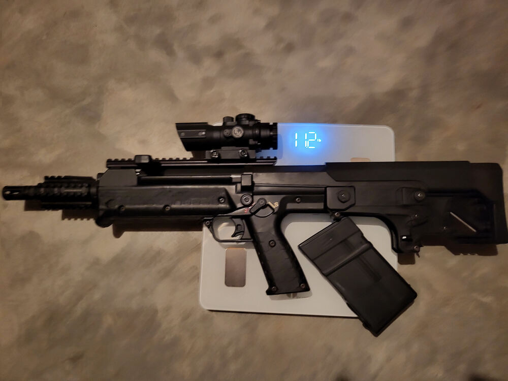 A KelTec RFB with scope, Picatinny rail barrel  attachment, and a Thermold magazine on a scale showing 11.2 lbs, unloaded